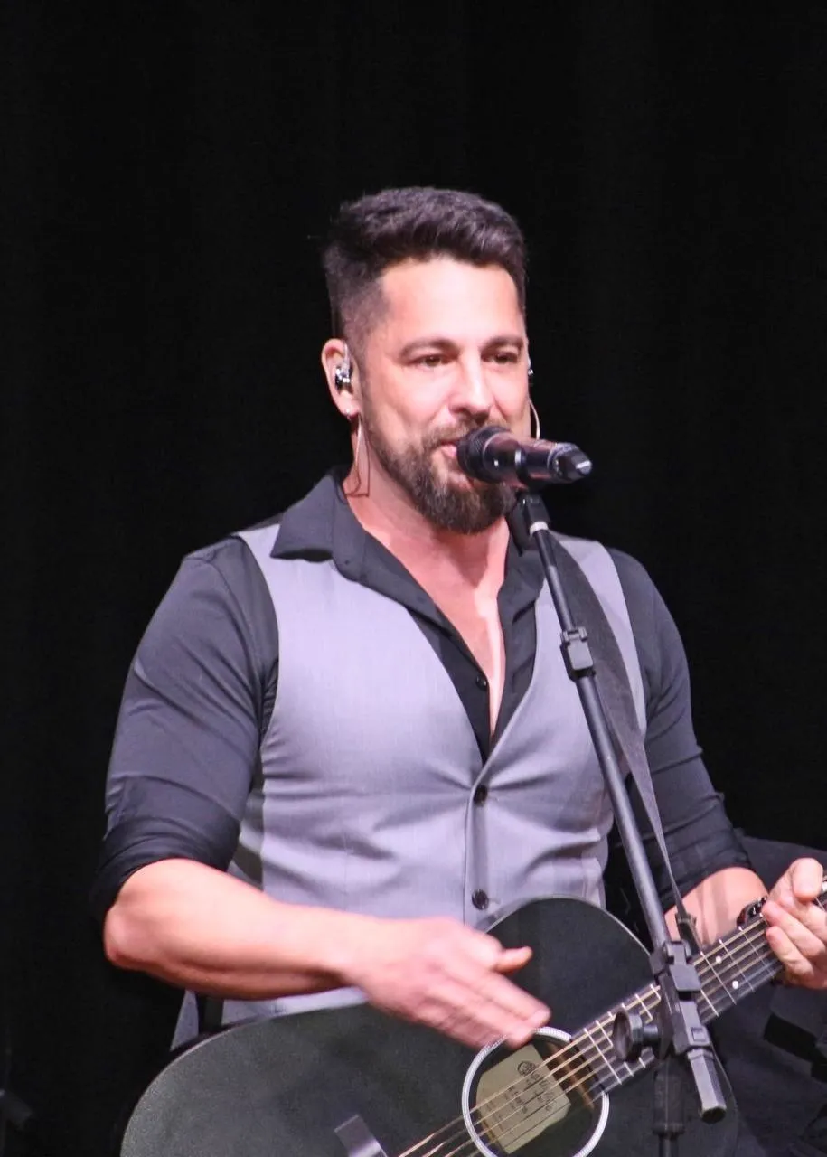 Dani Vendramini sorrindo no palco com o violão